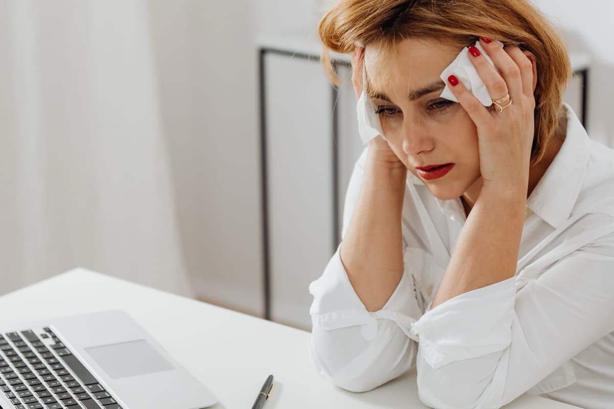Woman at her desk looking flushed and uncomfortable, dabbing her face