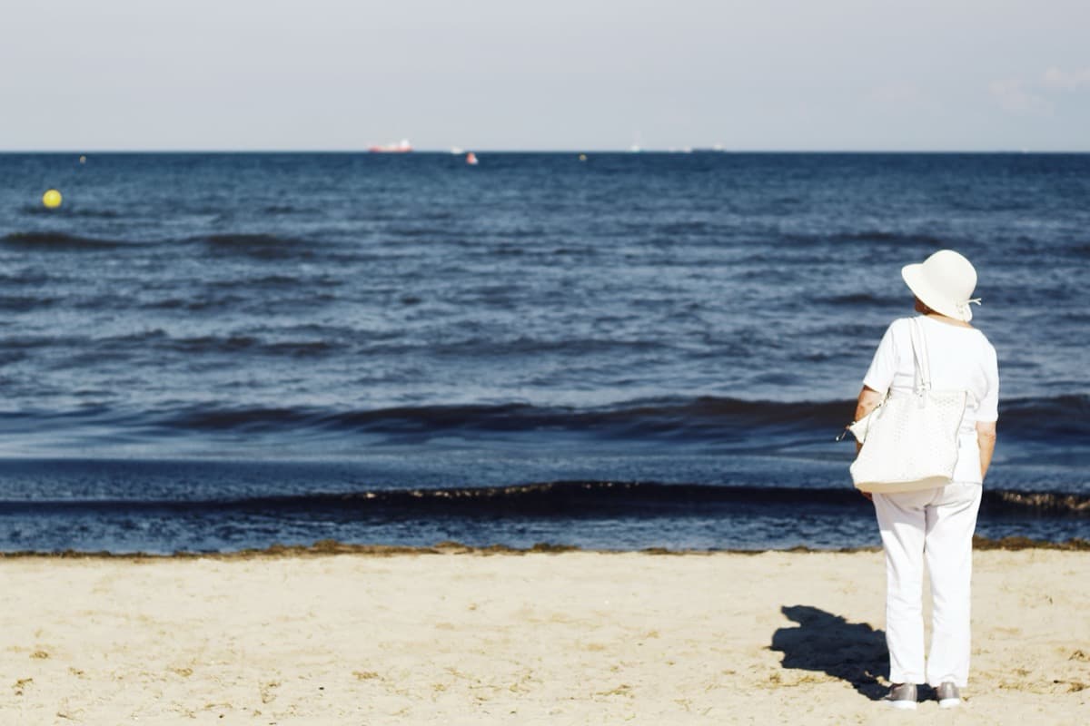 Woman standing quietly at the edge of the sea, looking out at the horizon