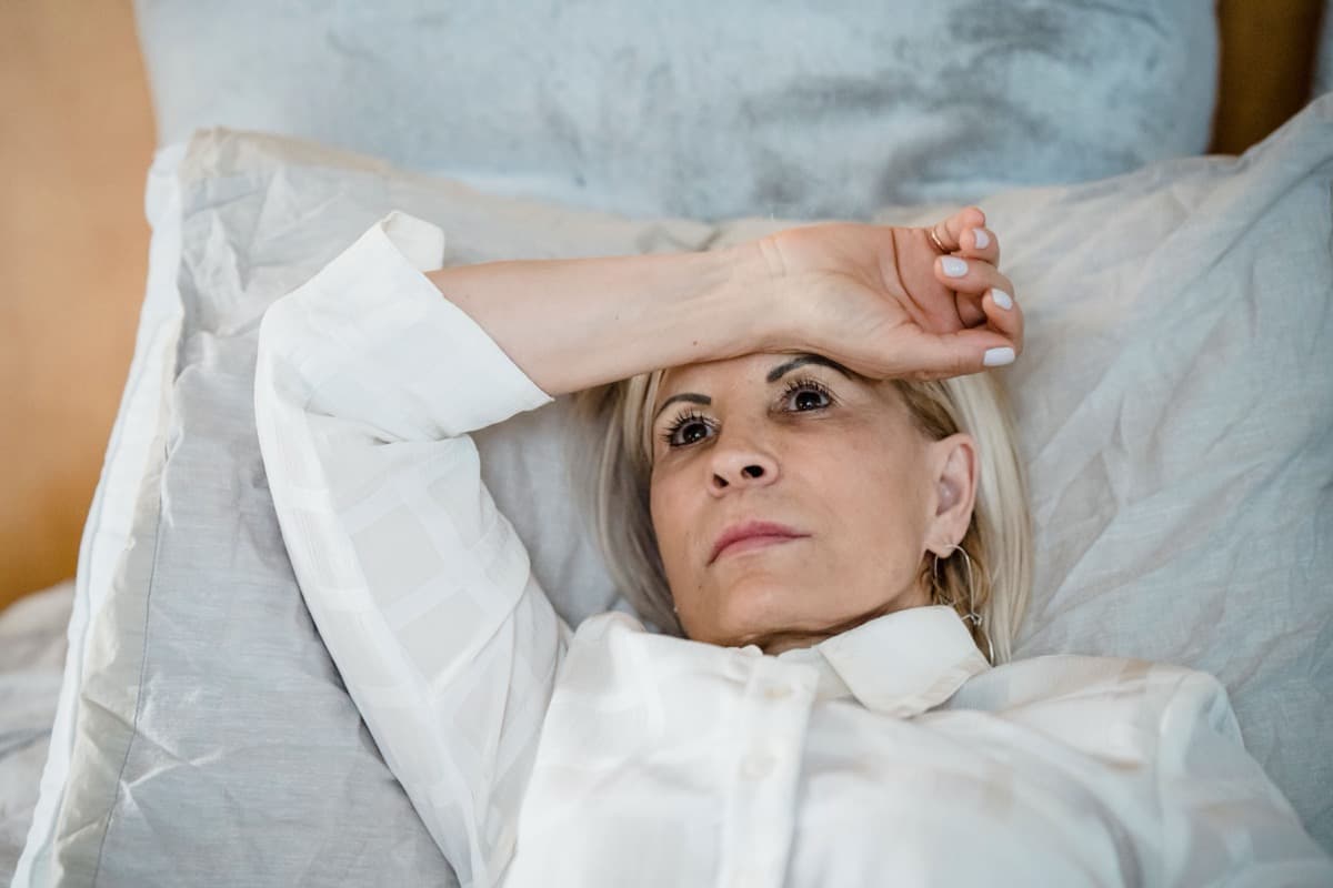 Woman lying awake in bed at night, eyes open, arm over her forehead