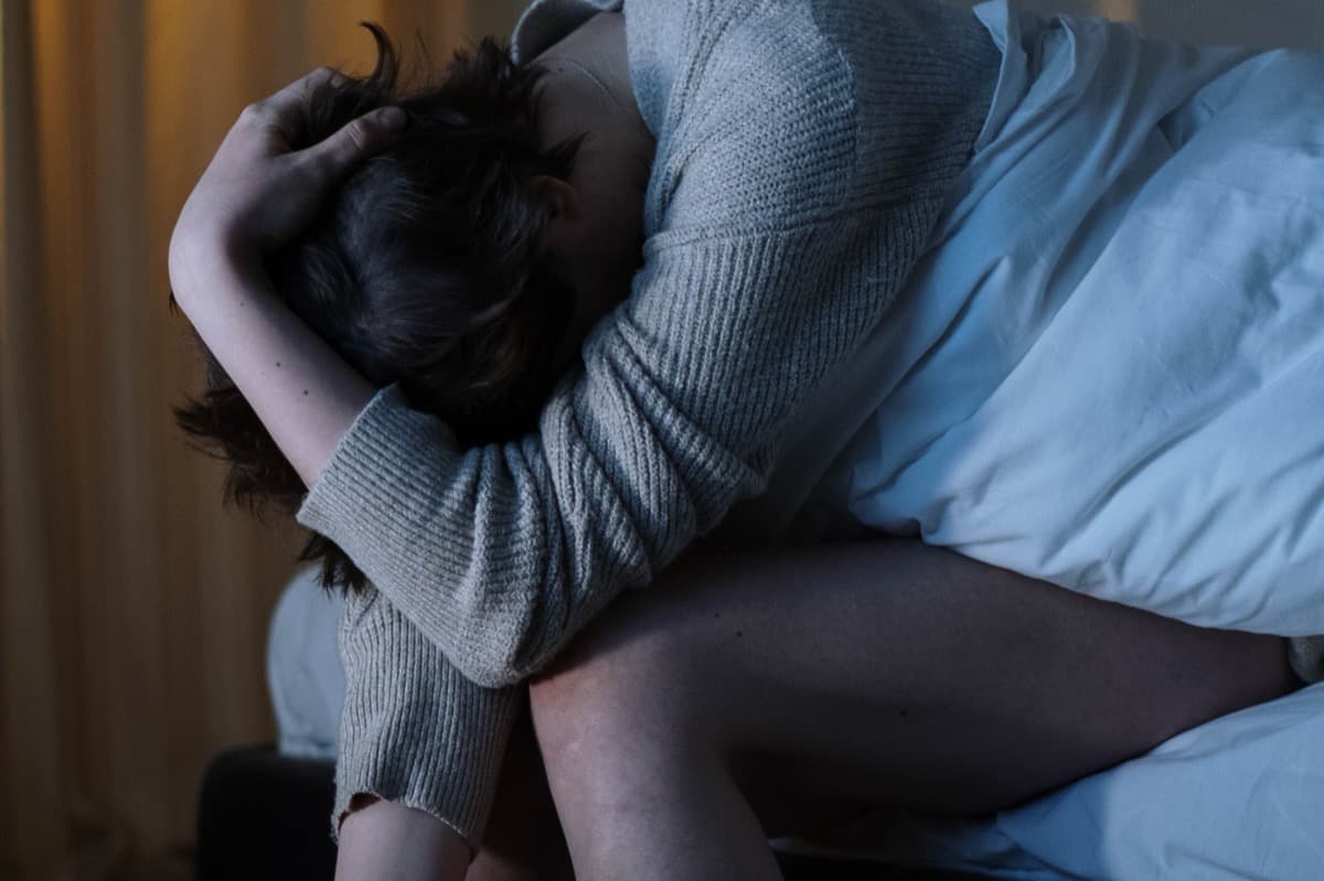 Woman sitting on the edge of her bed at night, unable to sleep