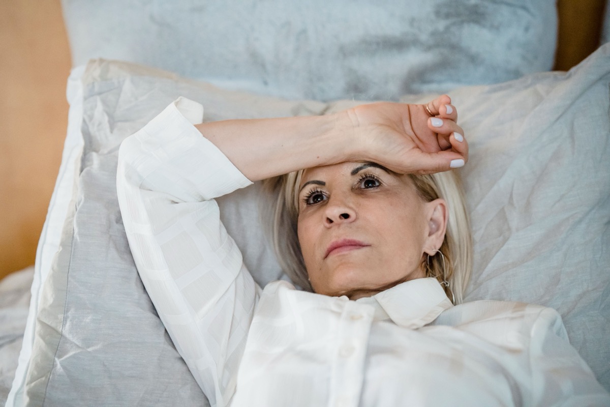 Woman lying awake in bed at night, eyes open, arm over her forehead